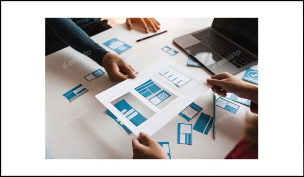 Personas trabajando en el diseño de una página web con esquemas y maquetas en papel sobre una mesa, representando la organización del contenido visual.