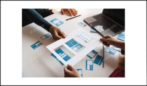 Personas trabajando en el diseño de una página web con esquemas y maquetas en papel sobre una mesa, representando la organización del contenido visual.