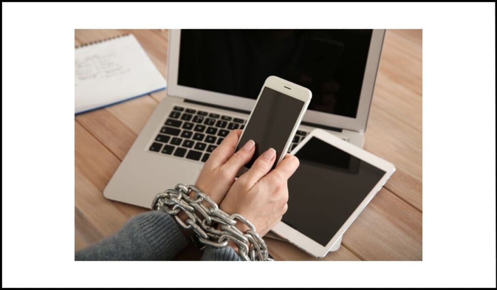 Manos encadenadas sujetando un teléfono móvil frente a una laptop y una tablet, simbolizando la restricción de interacción solo al tacto en dispositivos con pantalla táctil.